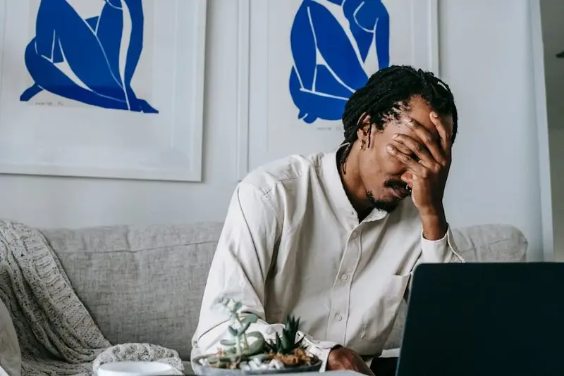 Frustrated young bearded African American male freelancer with dreadlocks in casual shirt working on