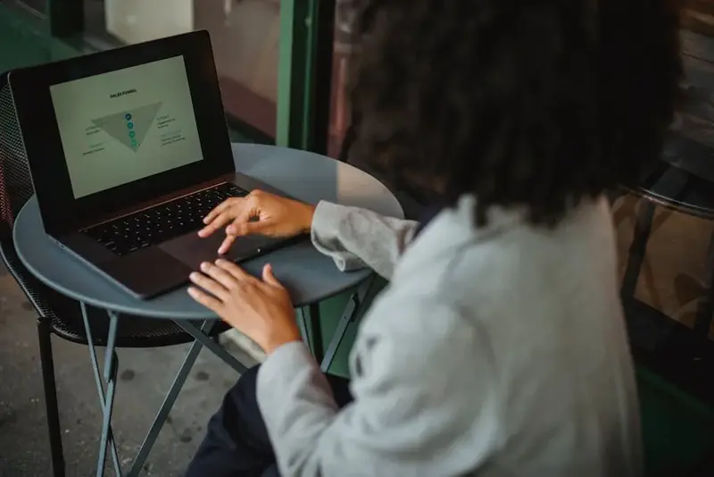 Back view of anonymous ethnic female in suit working with chart on computer while sitting at table i