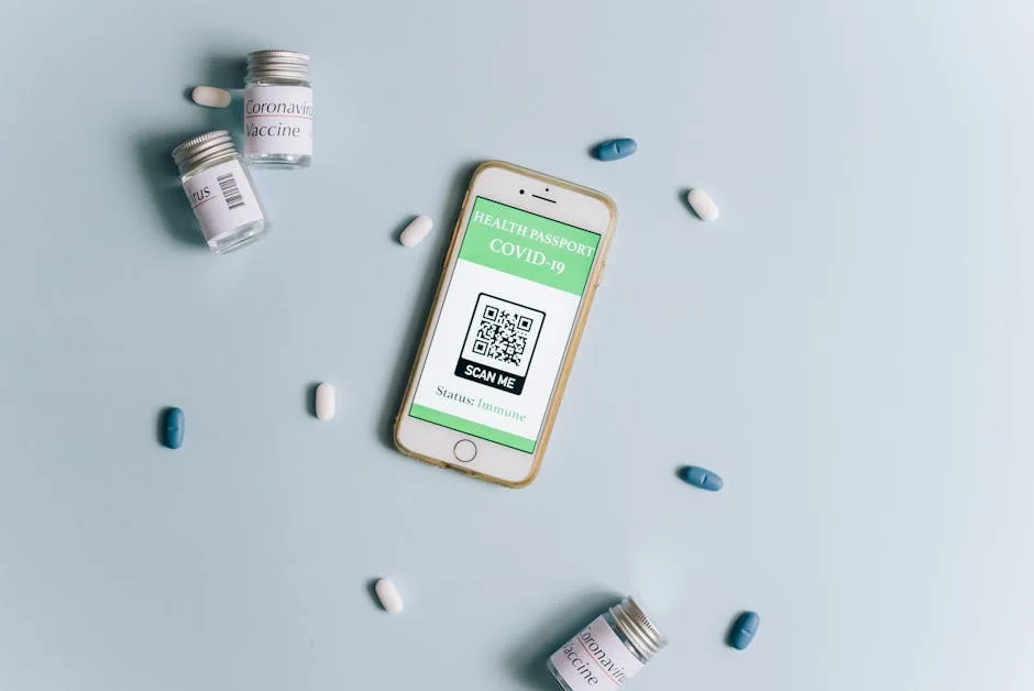 Image of a smartphone displaying a health passport alongside COVID-19 vaccine vials and pills on a l